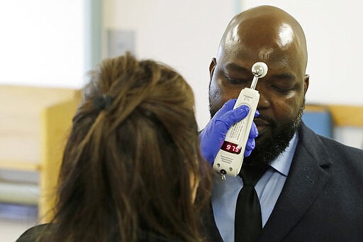 Relwende Guiguemde, right, has his temperature taken by Angie Webb, left, a nurse at Western State Hospital, Thursday, March 19, 2020, as he arrives at a visitors' entrance for a job interview in Lakewood, Wash. A patient and a worker at the facility, Washington state's largest psychiatric hospital, have tested positive for the new coronavirus. (AP Photo/Ted S. Warren)