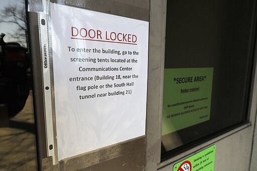 A sign at a locked entrance to Western State Hospital directs employees to go to another entrance where they may be screened for symptoms of the new coronavirus, Thursday, March 19, 2020, in Lakewood, Wash. A patient and a worker at the facility, Washington state's largest psychiatric hospital, have tested positive for COVID-19. (AP Photo/Ted S. Warren)