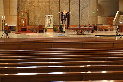 Los Angeles Archbishop Jose Gomez, left, prays the rosary to an empty hall at the Cathedral of Our Lady of the Angels as TV cameras sit at left and right, Thursday, March 19, 2020, in Los Angeles. The prayer, which was broadcast, was done in conjunction with Pope Francis who urged Catholics to unite spiritually to pray the rosary simultaneously on the Feast of St. Joseph. While services are normally broadcast, the televising of services has become especially important since the archdiocese has had to close their doors to parishioners due to the coronavirus. (AP Photo/Mark J. Terrill)