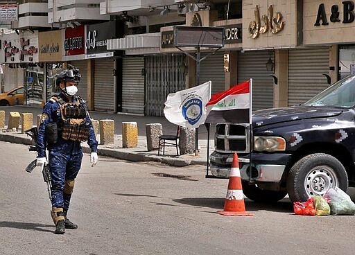 A federal policeman mans a checkpoint near shops that are shuttered to help prevent the spread of the coronavirus, in Baghdad, Iraq, Thursday, March 19, 2020. Iraq announced a weeklong curfew to help fight the COVID-19 pandemic. (AP Photo/Hadi Mizban)