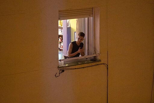 FILE - In this March 15, 2020, file photo, a man applauds from his window in support of the medical staff in Madrid, Spain.  At a time of unfathomable isolation, people in many European cities hit hard by the new coronavirus are taking at least a minute to come together in gratitude as they stand at open windows or on balconies singing, cheering and applauding. (AP Photo/Paul White, File)