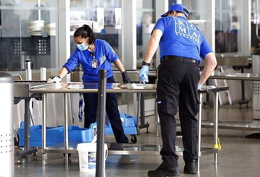 FILE - In this March 14, 2020 file photo, a cleaning crew wipes down table surfaces at the Transportation Security Administration's checkpoint at Terminal 5 at New York's John F. Kennedy International Airport. As the global viral pandemic grows, the need for cleaning and disinfecting has surged. Cleaners and domestic workers are essential in the effort to contain the virus. (AP Photo/Kathy Willens, File)