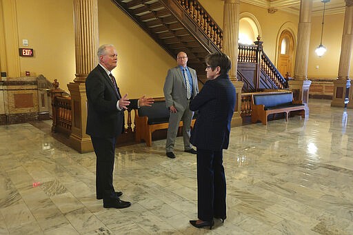 Kansas state Sen. Gene Suellentrop, left, R-Wichita, speaks with Democratic Gov. Laura Kelly, right, outside her Statehouse office, as her security officer watches, Thursday, March 19, 2020, in Topeka, Kan. Kelly is practicing social distancing during the coronavirus pandemic. (AP Photo/John Hanna)