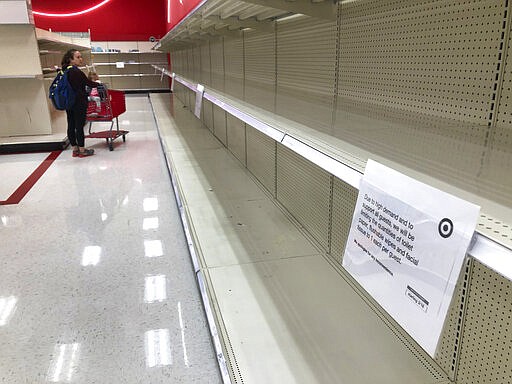 A woman looks at empty shelves in the paper goods section at a Target store Thursday, March 19, 2020, in Overland Park, Kan. Stores continue to struggle to keep shelves stocked with toilet paper, face masks, hand sanitizer, disinfectants and other items as people panic shop in response to the coronavirus pandemic. (AP Photo/Charlie Riedel)