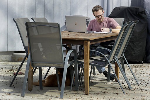 Erik Wray works on his computer in the backyard of his home Thursday, March 19, 2020, in Overland Park, Kan. Wray, a program manager for the Alzheimer's Association - Heart of America chapter, is among millions of workers toiling from home in an attempt to stem the spread of the coronavirus. (AP Photo/Charlie Riedel)