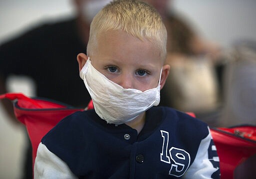 A boy wears a mask as he waits to travel from O.R.Tambo Airport in Johannesburg, South Africa, Thursday, March 19, 2020.  As more African countries closed their borders, the coronavirus' local spread threatened to turn the continent of 1.3 billion people into an alarming new front for the pandemic. For most people the virus causes only mild or moderate symptoms. For others it can cause more severe illness, especially in older adults and people with existing health problems. (AP Photo/Denis Farrell)