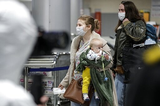 A passengers wearing face mask with her baby walks to medical experts to be checked after arriving from a foreign country at Sheremetyevo airport outside Moscow, Russia, Thursday, March 19, 2020. Authorities in Russia are taking vast measures to prevent the spread of the disease in the country. The measures include closing the border for all foreigners, shutting down schools for three weeks, sweeping testing and urging people to stay home. For most people, the new coronavirus causes only mild or moderate symptoms. For some it can cause more severe illness. (AP Photo/Pavel Golovkin)