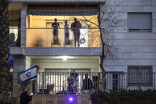 Israeli families stand on their balconies and applaud to their medical teams fighting the coronavirus outbreak in the town of Ashkelon, Israel, Thursday, March 19, 2020. (AP Photo/Tsafrir Abayov)