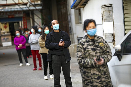 In this March 18, 2020 photo, people stand in a spaced line as they wait to buy pork at the entrance gate of a closed residential community in Wuhan in central China's Hubei Province. Last month, Wuhan was overwhelmed with thousands of new cases of coronavirus each day. But in a dramatic development that underscores just how much the outbreak has pivoted toward Europe and the United States, Chinese authorities said Thursday that the city and its surrounding province had no new cases to report. The virus causes only mild or moderate symptoms, such as fever and cough, for most people, but severe illness is more likely in the elderly and people with existing health problems. (Chinatopix via AP)