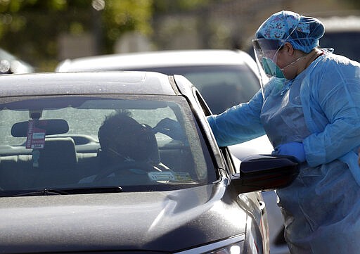 A man is swabbed as he is tested for COVID-19 as vehicles line up at the Doris Ison Health Center, Wednesday, March 18, 2020, in Miami. The testing is being provided by Community Health of South Florida, Inc.  According to the World Health Organization, most people recover in about two to six weeks, depending on the severity of the illness. (AP Photo/Lynne Sladky)