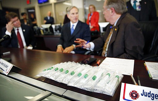 A group of coronavirus specimen collection units sit on the desk where Texas Governor Greg Abbott, center, addressed the coronavirus death of Patrick James who resided at the Texas Masonic Retirement Center. The press conference was held in the Arlington Emergency Management office in Arlington, Wednesday March 18, 2020. (Tom Fox/The Dallas Morning News via AP)