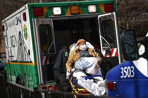 A patient wears a protective face mask as she is loaded into an ambulance at The Brooklyn Hospital Center emergency room, Wednesday, March 18, 2020, in New York. Anticipating a spike in coronavirus patients, New York City-area hospitals are clearing out beds, setting up new spaces to triage patients and urging people with mild symptoms to consult health professionals by phone or video chat instead of flooding emergency rooms that could be overrun. (AP Photo/John Minchillo)