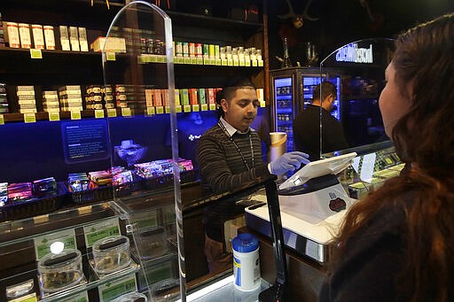 Max de Leon, a budtender at The Green Cross cannabis dispensary, center, wears gloves while helping customer Alex Luna in San Francisco, Wednesday, March 18, 2020. Marijuana stores in San Francisco remained open, as usual, Wednesday. (AP Photo/Jeff Chiu)