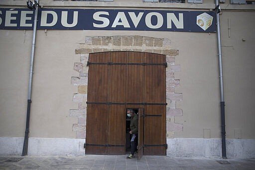 In this photo taken Monday March 16, 2020, Serge Bruna locks up the Marseille soap museum on the Old Port in Marseille, southern France. Amid the rapid outbreak of the new coronavirus across Europe, the hallmark Marseille tradition of soap-making is enjoying a renaissance, as the French public rediscovers this essential local product. As French shops were ordered closed this week in a bid to counter the new coronavirus, Bruna's Savonnerie de la Licorne now runs its operations only for delivery, supplying pharmacies across France and handling individual orders placed through its online store. (AP Photo/Daniel Cole)