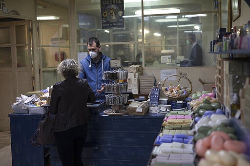 In this photo taken Monday March 16 2020 a factory worker wears a mask as he attends to a customer at the Licorne soap factory in Marseille, southern France. Amid the rapid outbreak of the new coronavirus across Europe, the hallmark Marseille tradition of soap-making is enjoying a renaissance, as the French public rediscovers this essential local product. As French shops were ordered closed this week in a bid to counter the new coronavirus, Bruna's Savonnerie de la Licorne now runs its operations only for delivery, supplying pharmacies across France and handling individual orders placed through its online store. (AP Photo/Daniel Cole)