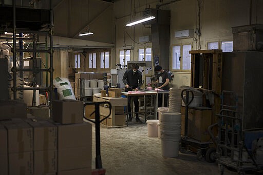 In this photo taken Monday March 16 2020 workers wearing masks produce soap at the Licorne soap factory in Marseille, southern France. Amid the rapid outbreak of the new coronavirus across Europe, the hallmark Marseille tradition of soap-making is enjoying a renaissance, as the French public rediscovers this essential local product. As French shops were ordered closed this week in a bid to counter the new coronavirus, Bruna's Savonnerie de la Licorne now runs its operations only for delivery, supplying pharmacies across France and handling individual orders placed through its online store. (AP Photo/Daniel Cole)