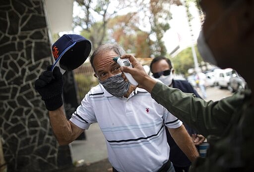 A man removes his cap as a soldier takes his temperature outside a food market as a preventative measure against the spread of the coronavirus in Caracas, Venezuela, Thursday, March 19, 2020. To enter the market, people are required to get their temperature taken and disinfect their hands. (AP Photo/Ariana Cubillos)