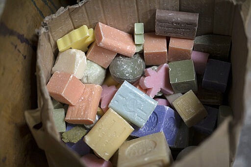 In this photo taken Monday March 16 2020 discarded bars of soap sit in a bucket at the Licorne soap factory in Marseille, southern France. Amid the rapid outbreak of the new coronavirus across Europe, the hallmark Marseille tradition of soap-making is enjoying a renaissance, as the French public rediscovers this essential local product. As French shops were ordered closed this week in a bid to counter the new coronavirus, Bruna's Savonnerie de la Licorne now runs its operations only for delivery, supplying pharmacies across France and handling individual orders placed through its online store. (AP Photo/Daniel Cole)