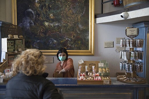 In this photo taken Monday March 16, 2020, Julie Dinot wears a mask as she attends to customers at the Savonnerie de la Licorne shop on Marseille's Old Port in Marseille, southern France. Amid the rapid outbreak of the new coronavirus across Europe, the hallmark Marseille tradition of soap-making is enjoying a renaissance, as the French public rediscovers this essential local product. For most people, the new coronavirus causes only mild or moderate symptoms. For some it can cause more severe illness. (AP Photo/Daniel Cole)
