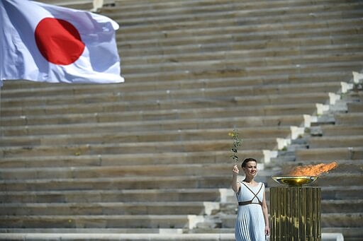 Choreographer Artemis Ignatiou stands next to the Olympic flame during the Olympic flame handover ceremony for the 2020 Tokyo Summer Olympics, in Athens, Thursday March 19, 2020. (Aris Messinis/Pool via AP)