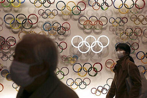 FILE - In this Feb. 23, 2020, file photo, two people wear masks as they visit the newly opened Japan Olympic Museum located near the New National Stadium in Tokyo. The Olympic flame from Greece is set to arrive in Japan even as the opening of the the Tokyo Games in four months is in doubt with more voices suggesting the games should to be postponed or canceled because of the worldwide virus pandemic. (AP Photo/Jae C. Hong, File)