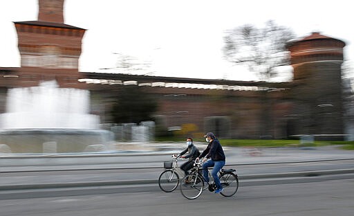 People wearing protective mask ride their bicycle at the Castello Sforzesco castle in Milan, Italy, Thursday, March 19, 2020.For most people, the new coronavirus causes only mild or moderate symptoms. For some it can cause more severe illness, especially in older adults and people with existing health problems. (AP Photo/Antonio Calanni)