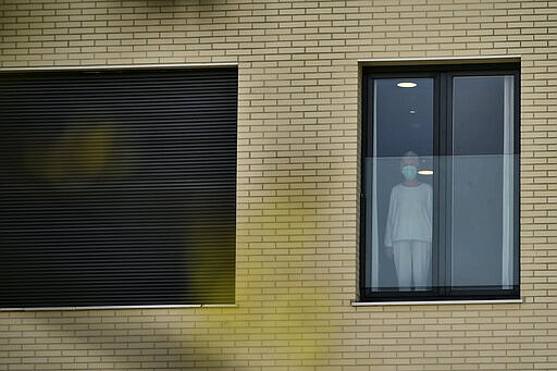 A woman wearing protection mask looks on through the window, at San Martin nursing home, where several elderly people were infected by coronavirus in Vitoria, northern Spain, Thursday, March 19, 2020. Spain will mobilize 200 billion euros or the equivalent to one fifth of the country's annual output in loans, credit guarantees and subsidies for workers and vulnerable citizens, Prime Minister Pedro Sanchez announced Tuesday. For most people, the new coronavirus causes only mild or moderate symptoms. For some, it can cause more severe illness, especially in older adults and people with existing health problems. (AP Photo/Alvaro Barrientos)