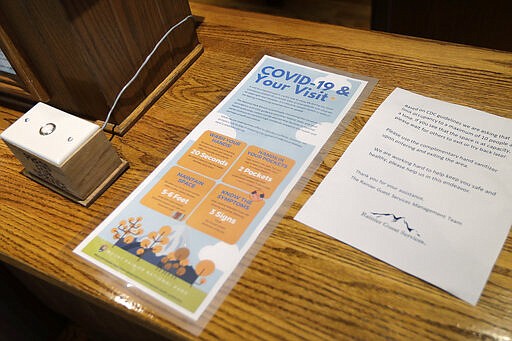 Signs at the reception desk at the National Park Inn at Longmire offer tips to prevent the spread of the COVID-19 virus and ask that guests limit use of a sitting area to 10 people or fewer, at Mount Rainier National Park, Wednesday, March 18, 2020, in Washington state. Most national parks are remaining open during the outbreak of the new coronavirus, but many are closing visitor centers, shuttles, lodges and restaurants in hopes of containing its spread. (AP Photo/Ted S. Warren)