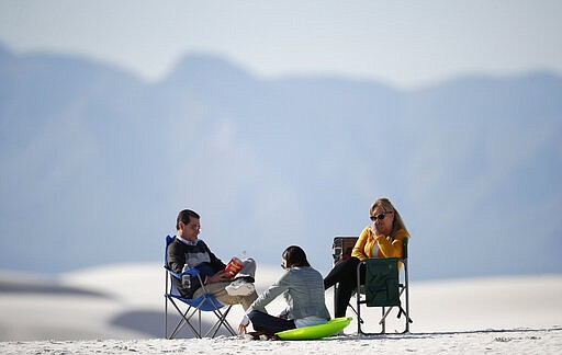 In this March 5, 2020, photograph, visitors relax on a gypsum dune in White Sands National Park at Holloman Air Force Base, N.M. Most national parks are open as a refuge for Americans tired of being stuck at home because of the coronavirus. Entry fees have been eliminated, but many parks are closing visitor centers, shuttles and lodges to fight the spread of the virus. (AP Photo/David Zalubowski)