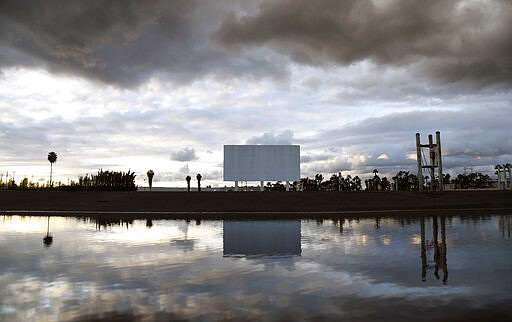 A movie screen at the Paramount Drive-In Theatres is reflected in rainwater before opening, Thursday, March 19, 2020, in Paramount, Calif. The theatre was scheduled to shut down Friday after California Gov. Gavin Newsom issued a statewide stay-at-home order due to the coronavirus. (AP Photo/Chris Pizzello)