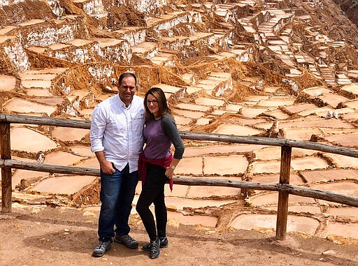 In a photo provided by Linda Scruggs and Mike Rustici, Linda Scruggs and Mike Rustici pose for a photo at salt mines outside Sacred Valley on March 15, 2020, in Peru, just before the Peruvian president announced the country was  going under lockdown. The two are trapped in a Lima hotel room and do not know when they will make it back to the U.S. The couple, like thousands around the world, are trapped as nations closed their borders to try to stop the spread of the new coronavirus.  (Linda Scruggs and Mike Rustici via AP)