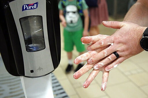 FILE - In this March 17, 2020, file photo, a traveler uses hand sanitizer from a dispenser at Sky Harbor Airport in Phoenix. The Associated Press has found that the critical shortage of testing swabs, protective masks, surgical gowns and hand sanitizer can be tied to a sudden drop in imports of medical supplies. (AP Photo/Sue Ogrocki)