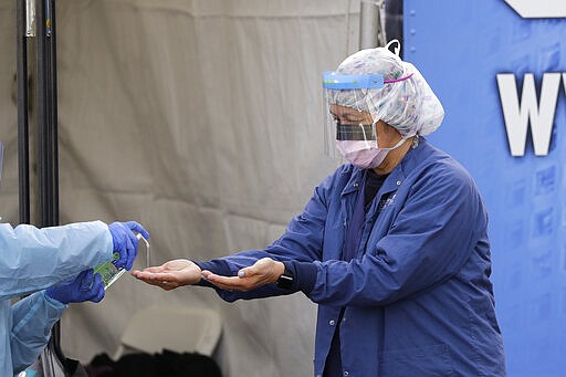 In this March 17, 2020, photo, Theresa Malijan, a registered nurse, has hand sanitizer applied on her hands after removing her gloves after she took a nasopharyngeal swab from a patient at a drive-through COVID-19 testing station for University of Washington Medicine patients in Seattle. The Associated Press has found that the critical shortage of testing swabs, protective masks, surgical gowns and hand sanitizer can be tied to a sudden drop in imports of medical supplies. (AP Photo/Elaine Thompson)