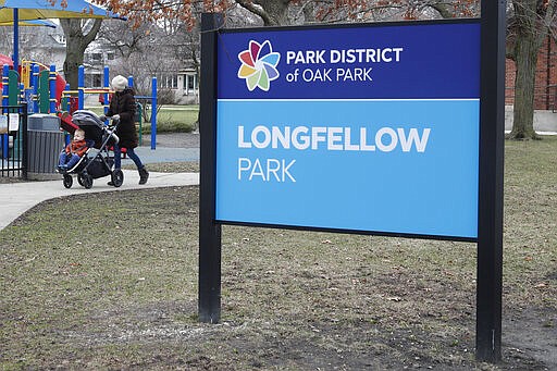 A resident of the Village of Oak Park, Ill., walks with a child in Longfellow Park, Friday, March 20, 2020. There are at least three confirmed cases of COVID-19 in Oak Park, just nine miles from downtown Chicago, where the mayor has ordered residents to shelter in place. With so few tests available, surely there are others, says Tom Powers, spokesman for the village of about 52,000 in a metropolitan area with millions. (AP Photo/Charles Rex Arbogast)