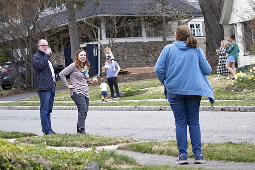 Residents of Brookfield Road in Montclair, N.J., get together for a street happy hour toast Friday, March 20, 2020. With bars shuttered and stressed-out workers stuck at home, companies and friend groups across the U.S. are holding happy hours over video chat to commiserate and keep spirits high amid the new coronavirus pandemic. In one community, neighbors are toasting to one another every night from the ends of their driveways to unwind &#151; while keeping a safe distance, of course. (AP Photo/Mary Altaffer)