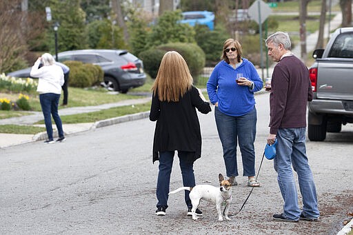 Residents of Brookfield Road in Montclair, N.J., get together for a street happy hour toast Friday, March 20, 2020. With bars shuttered and stressed-out workers stuck at home, companies and friend groups across the U.S. are holding happy hours over video chat to commiserate and keep spirits high amid the new coronavirus pandemic. In one community, neighbors are toasting to one another every night from the ends of their driveways to unwind &#151; while keeping a safe distance, of course. (AP Photo/Mary Altaffer)