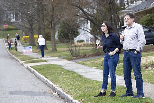 Residents of Brookfield Road in Montclair, N.J., get together for a street happy hour toast Friday, March 20, 2020. With bars shuttered and stressed-out workers stuck at home, companies and friend groups across the U.S. are holding happy hours over video chat to commiserate and keep spirits high amid the new coronavirus pandemic. In one community, neighbors are toasting to one another every night from the ends of their driveways to unwind &#151; while keeping a safe distance, of course. (AP Photo/Mary Altaffer)