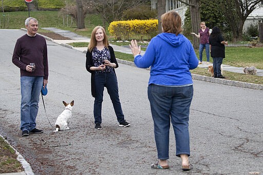 Residents of Brookfield Road in Montclair, N.J., get together for a street happy hour toast Friday, March 20, 2020. With bars shuttered and stressed-out workers stuck at home, companies and friend groups across the U.S. are holding happy hours over video chat to commiserate and keep spirits high amid the new coronavirus pandemic. In one community, neighbors are toasting to one another every night from the ends of their driveways to unwind &#151; while keeping a safe distance, of course. (AP Photo/Mary Altaffer)