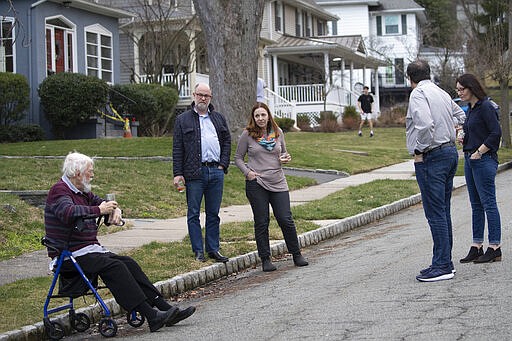 Residents of Brookfield Road in Montclair, N.J., get together for a street happy hour toast Friday, March 20, 2020. With bars shuttered and stressed-out workers stuck at home, companies and friend groups across the U.S. are holding happy hours over video chat to commiserate and keep spirits high amid the new coronavirus pandemic. In one community, neighbors are toasting to one another every night from the ends of their driveways to unwind &#151; while keeping a safe distance, of course. (AP Photo/Mary Altaffer)