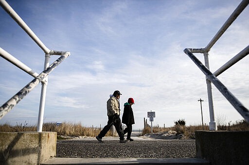 Pedestrians walk along the shore in Cape May, N.J., Wednesday, March 18, 2020. Some people who live in cities or their suburbs have been fleeing to their second homes at the shore to ride out the coronavirus near the beach. But neighbors in many of those towns are yanking the welcome mat, fearing infection and an overwhelming of already-stretched resources. (AP Photo/Matt Rourke)