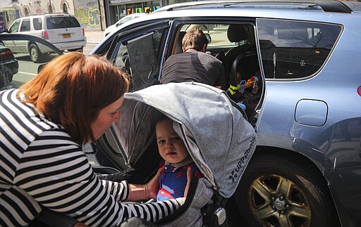 While Justin Bracken packs the family car, Cailin Sandvig, left, lifts their 10-month old son Milo from his stroller to join his twin inside the car, as they prepare to leave home in the Crown Heights neighborhood of the Brooklyn borough of New York to avoid the spread COVID-19, Monday March 16, 2020. &quot;We are fleeing the city,&quot; said Sandvig who works remotely for her job. &quot;We are going to end up in Wheaton, Illinois, where we have a big old house to be in with my mom that's otherwise empty.&quot; Bracken added that from following the news &quot;its been clear for a while that things are getting pretty serious&#151;especially from Italy, it seems pretty eminent that things are about to get bad here.&quot; (AP Photo/Bebeto Matthews)