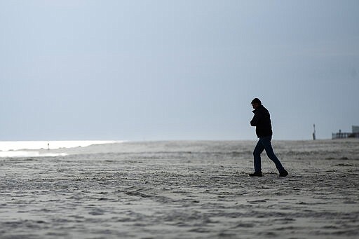 A person walks toward the ocean in Cape May, N.J., Wednesday, March 18, 2020. Some people who live in cities or their suburbs have been fleeing to their second homes at the shore to ride out the coronavirus near the beach. But neighbors in many of those towns are yanking the welcome mat, fearing infection and an overwhelming of already-stretched resources. (AP Photo/Matt Rourke)