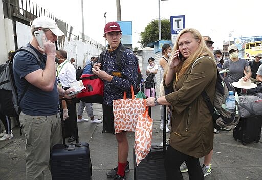 Tourists from the United States wait outside the closed Jorge Chavez International Airport for a member of the U.S. Embassy to escort them to a flight that will fly them back to the U.S., in Callao Peru, Friday, March 20, 2020, on the fifth day of a state of emergency decreed by the government to prevent the spread of the new coronavirus.  (AP Photo/Martin Mejia)