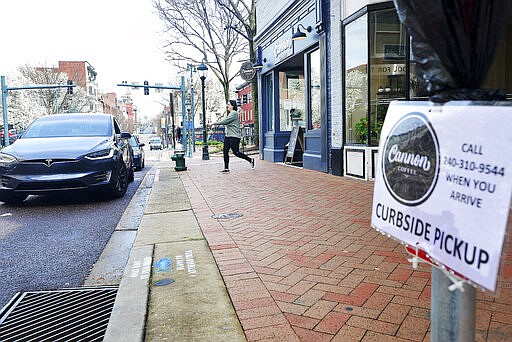 Elie Nogle, a barista at Cannon Coffee, waits on customers parked outside the coffee shop in downtown Hagerstown, Md., Thursday, March 19, 2020. Customers can order online and call when they arrive to pick up thier order.  (Colleen McGrath/The Herald-Mail via AP)