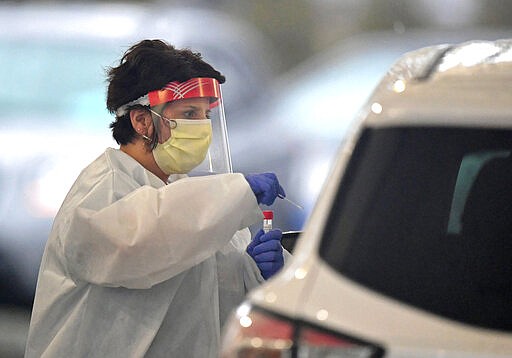 Nurse practitioner April Sweeney takes a sample from a patient, Friday, March 20, 2020, at the drive-through testing site at the AHN Health + Wellness Pavilion, in Millcreek Township, near Erie, Pa. . Saint Vincent Hospital officials expected to test up to 40 patients daily at the site, which opened Friday.   The samples will be tested for flu strains before they're tested for COVID-19, a new coronavirus. (Christopher Millette/Erie Times-News via AP)