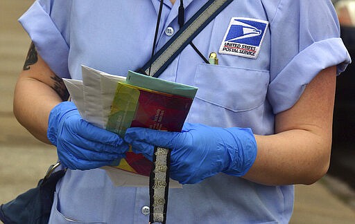 A U.S Postal Service mail carrier wears gloves while delivering mail, Friday March 20, 2020, in South Wilkes-Barre, Pa. (Aimee Dilger/The Times Leader via AP)