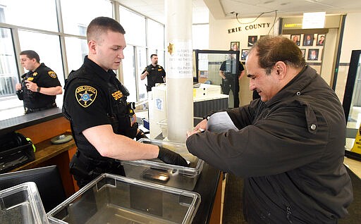 Erie County Sheriff's Deputy Jonathan Clover assists Shahram Abdollahi, of Erie, Pa., before he passes through a metal detector Thursday, March 19, 2020, at the front entrance of the Erie County Courthouse in Erie, Pa.. Much of the county's court business is shut down through at least early April under a Pennsylvania Supreme Court order issued on Wednesday in response to COVID-19, the new coronavirus. (Jack Hanrahan/Erie Times-News via AP)