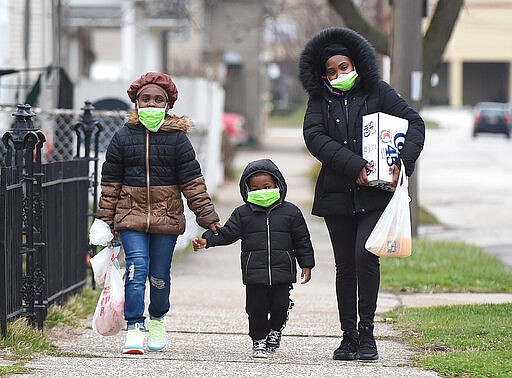 Marla Beason of Erie, and her children Samori, 8, left, and Durrell, 4, walk March 20, 2020, to their home in the 300 block of West 17th Street in Erie after shopping at a nearby store. Beason said her family started wearing the face masks recently because of COVID-19, the new coronavirus. She said they are taking other precautions like frequent hand washing and social distancing. (Jack Hanrahan/Erie Times-News via AP)