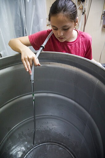 Olivia Newton, 11, pours alcohol into a vat normally used to infuse vodka, in order to create hand sanitizer inside of Lass and Lions' manufacturing facility on Thursday, March 19, 2020 in Chattanooga, Tenn. Lass and Lions vodka distillers normally uses the location to infuse their product with flavors, but has recently began to work on creating 65% alcohol hand sanitizer to help Hamilton County residents in response to the national outbreak of coronavirus creating a shortage in the market. (Troy Stolt/Chattanooga Times Free Press via AP)