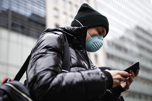 Pedestrian uses her phone while wearing a face mask in Herald Square, Thursday, March 12, 2020, in New York. New York City Mayor Bill de Blasio said Thursday he will announce new restrictions on gatherings to halt the spread of the new coronavirus in the coming days, but he hopes to avoid closing all public events such as Broadway shows. For most people, the new coronavirus causes only mild or moderate symptoms. For some it can cause more severe illness. (AP Photo/John Minchillo)